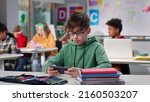 Small photo of Teenage boy watching video on smartphone sitting at desk in class. Schoolboy using cellphone in classroom at school