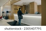 Small photo of Woman receptionist behind workplace in hotel lobby talking with guest. Businessman arrive to hotel and check in at reception
