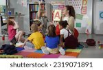 Small photo of Female teacher hold flashcard with letter a teaching preschool kids alphabet. Diverse pupils of primary school sit on floor with teacher having alphabet lesson