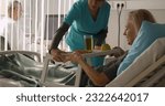 Small photo of Nurse serving senior female patient meal in hospital bed. Medical worker bringing tray with food for mature sick woman in hospital ward. Healthcare and medicine concept