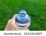 Small photo of First person point of view of plastic bottle of mineral water that is put in the mouth to drink. Selective focus on the spout of the plastic bottle and defocused natural background and copy space.