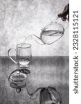 Small photo of Fluid transfusion from a teapot to a glass on a gray background