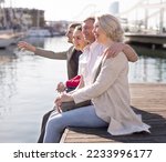 Small photo of group of tourists sitting on embankment dangling