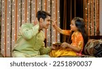 Small photo of Young siblings celebrating Raksha Bandhan or Bhai Dooj festival together - Happy family , Indian Model. Pretty sister happily putting tika on her elder brother's forehead in traditional wear
