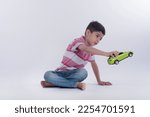 Small photo of Little boy sitting and playing with a green toy car - Childhood, young years. A happy boy is sitting on the floor and playing with toys with white background - Learning and Education background