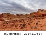 Small photo of Overton, Nevada, USA - February 25, 2010: Valley of Fire. Heavy rainy gray cloudscape gathers over red rock mountainous outcrop rising out of dry red desert floor with greenish shrubs.