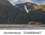 Small photo of Disenchantment Bay, Alaska, USA - July 21, 2011: Snow collects in valley formed on mountain flank under blue cloudscape. Forested flanks all the way to ocean water with floating ice pieces