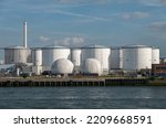 Small photo of Rotterdam, Netherlands - July 11, 2022: Chevron white oil and gas tanks under blue cloudscape with red stone office building. Shell chimney on horizon