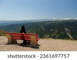 A Muslim woman in a black niqab sits on a bench and looks at the mountains from the back. Horizontal photo