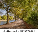 Small photo of York, UK. October 1, 2021. A footpath by a river bank in early autumn. A bridge and a tour boat are in the distance and trees overarch the path.