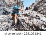 View from the back looking up at woman mountaineer in shorts climbing up on via ferrata trail in the Alps