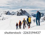 View from the back, five mountaineers descending down the snowy mountain, walking in a row 