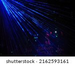 Bright blue neon rays against the background of multi-colored lights glowing in the dark. Laser show. Blurred image