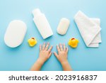 Small photo of Baby hands, white shampoo bottle, soap bar, towel, wisp and yellow rubber ducks on light blue table background. Pastel color. Closeup. Point of view shot. Things for baby bathing.