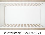 Empty baby crib with white mattress on wooden home floor. Closeup. Top view. 