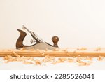 Small photo of Manual jointer and shavings on old wooden plank on white table at light gray wall background. Closeup. Preparing material for repair work of home. Side view.