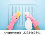 Small photo of Woman hands in rubber protective gloves holding white detergent bottle, sponge and washing steel grill grate for kitchen oven on light blue table background. Pastel color. Closeup. Point of view shot.