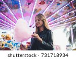 Adorable cute pretty woman stands in middle of amusement park, in front of ride with bright colours positive and cheerful, eats pink cotton candy floss, happy and optimistic