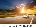 A silver crossover car driving fast on the countryside asphalt road against night sky with clouds and a beautiful sunset