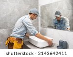 Small photo of Professional plumber, male worker in uniform installing sink and water pipe in new apartment