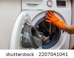 Small photo of Hand in torn glove cleaning the washing machine. Regular clean up. Maid cleans house.