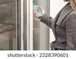 Woman locking smartlock on the entrance door using a smart phone. Concept of using smart electronic locks with keyless access.