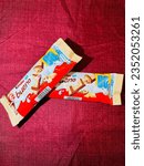 Small photo of Kinder bueno chocolate candy bar on maroon background. Kinder bueno by Italian confectionery manufacturer ferrero