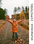 Small photo of Pensive ten years girl in orange coat with outstretched arms enjoys the fresh air in fall forest. Dry grass and golden trees. Autumn vibes, outdoor lifestyle. Emotional feeling, mental health