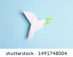 Paper origami dove of peace with olive branch on a blue background. World Peace Day concept.