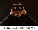 Small photo of man holding vhs tape, looking behind videocassette, isolated on black background.