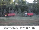 Small photo of Barcelona, Spain - October 28, 2023. Two red trucks in a forest, depicting industry's encroachment on nature