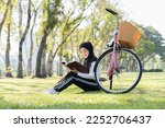 Asian young Muslim woman wear hijab black headscarf and hijab dress sitting and reading a book near bicycle in the park