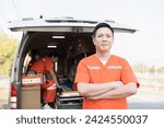 Small photo of Asian male ambulance staff member standing with crossed arms. He is wearing ambulance uniform of paramedics during paramedics giving injured person first aid background