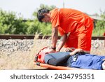 Small photo of Injured man on patient transport stretcher. Ambulance staff member assisting injured person with transport stretcher. Paramedics assisting injured person first aid on road