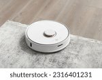 White robot vacuum cleaner on the carpet in the living room near the sofa. Cleaning the apartment with a modern smart vacuum cleaner.