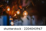 Small photo of Close up to bulb, light bokeh. Incandescent light bulb hanging In a night garden.