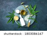Hemp leaves, oil, cosmetic products, face cream, body butter, face roller and gua sha massager on dark background. Top view, copy space. Natural skin and self care concept. Flat lay. Banner