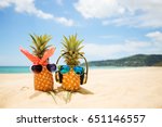 Couple of attractive pineapples in love on the sand against turquoise sea. Wearing stylish mirrored sunglasses. Tropical summer vacation concept. Sunny day on the beach of tropical island. Honeymoon