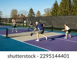 Small photo of A male player returns a volley at the net on a dedicated pickleball court at a public park.