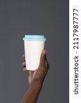 Small photo of African man hand with cardboard cup or disposable cup for coffee or tea. White disposable cup with blue plastic lead in mans hand. Disposable dishes concept. Copy space.