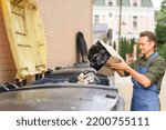Small photo of Throwing away unsorted trash employee man wearing apron put cardboard box with garbage plastic bag in it. Wrong unsorted garbage cans. Wrong way to throw your trash. Sorting garbage save the world.