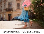 Summer street fashion details: elegant woman wearing trendy pink shirt with knot, polka dot blue midi skirt, white strap sandals, with yellow wicker leather shoulder bag, walking in street. Copy space