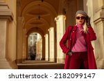 Small photo of Fashionable confident blonde woman wearing trendy sunglasses, beret, pink turtleneck cashmere sweater, dark red color autumn coat, gloves, posing in street of European city. Copy, empty space for text