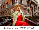 Happy smiling elegant woman wearing straw hat, red dress on Gondola ride in Venice, Italy. Travel, vacation, lifestyle conception. Copy, empty space for text