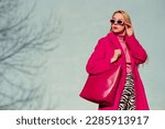Fashionable confident blonde woman wearing trendy pink sunglasses, fuchsia color coat, turtleneck, zebra print trousers,  holding faux leather tote, shopper bag. Copy, empty space for text