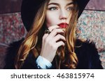 Outdoor portrait of a young beautiful fashionable lady wearing stylish black fur coat and wide-brimmed hat. Model looking aside. Female fashion concept. City lifestyle. Close up.