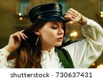 Outdoor close up portrait of young beautiful fashionable woman wearing stylish leather cap posing in street. Model closed eyes. Lights and reflections on background. Female fashion concept