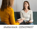 Young woman attentively listens to a psychologist at the reception, sitting on the couch in the office. Therapist consults the patient. Photo from the psychologist's back