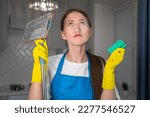 Small photo of Sad young woman in uniform looks up hopefully holding a mop and sponge in her hands. Unwillingness to clean the apartment, fatigue after cleaning