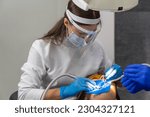 Small photo of Female dentist and assistant removing dental calculus from teeth. Visit is in proffessional dental clinic. Woman sits on dental chair. Drilling and treatment of tooth, filling.